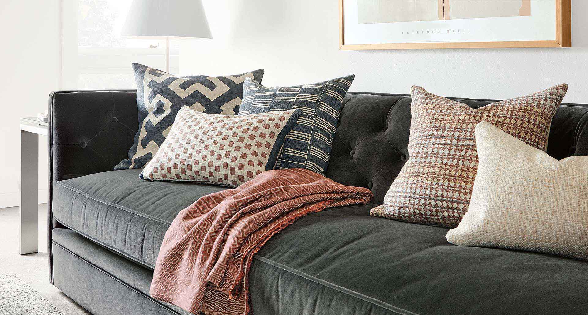 Four throw pillows of various patterns on a grey sofa
