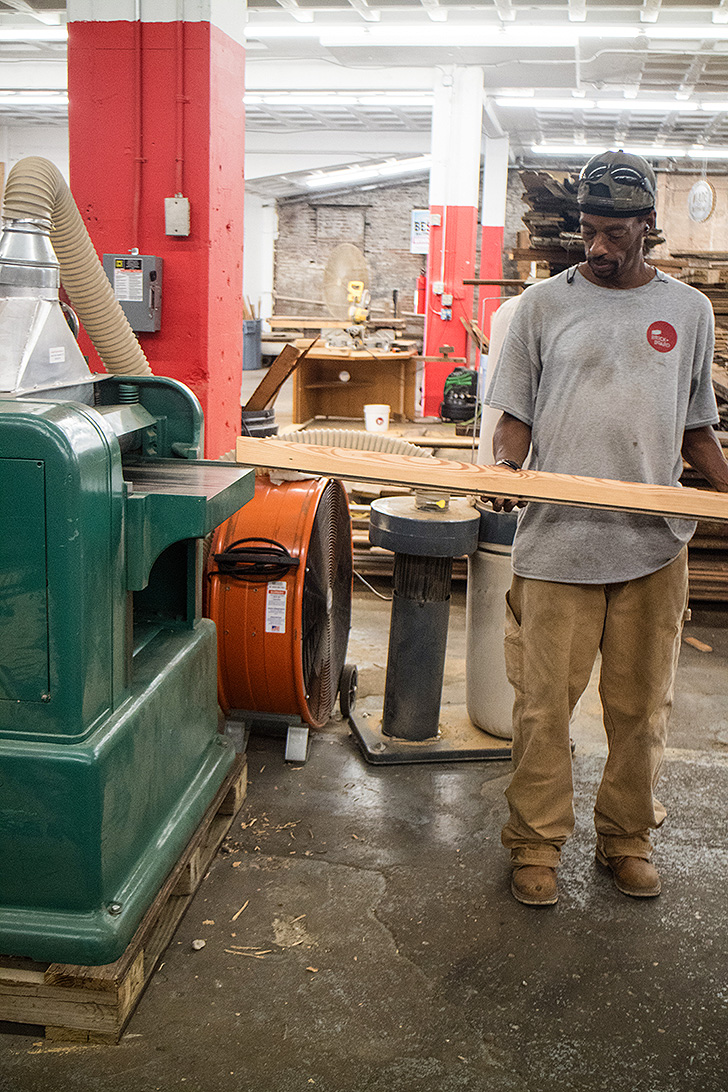 A woodworker takes reclaimed lumber through the planer