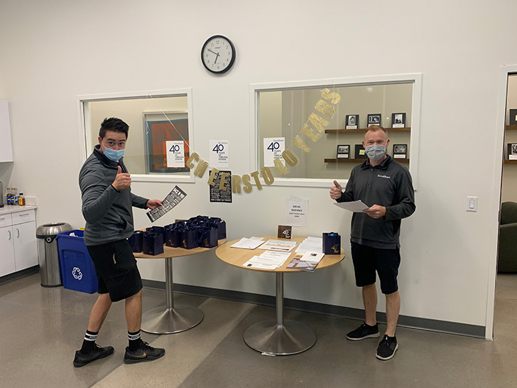 Two Denver Delivery Center staff members pose by a table with 40th anniversary items.