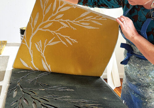 An artist is hand block-printing pillow fabric with a botanical image.